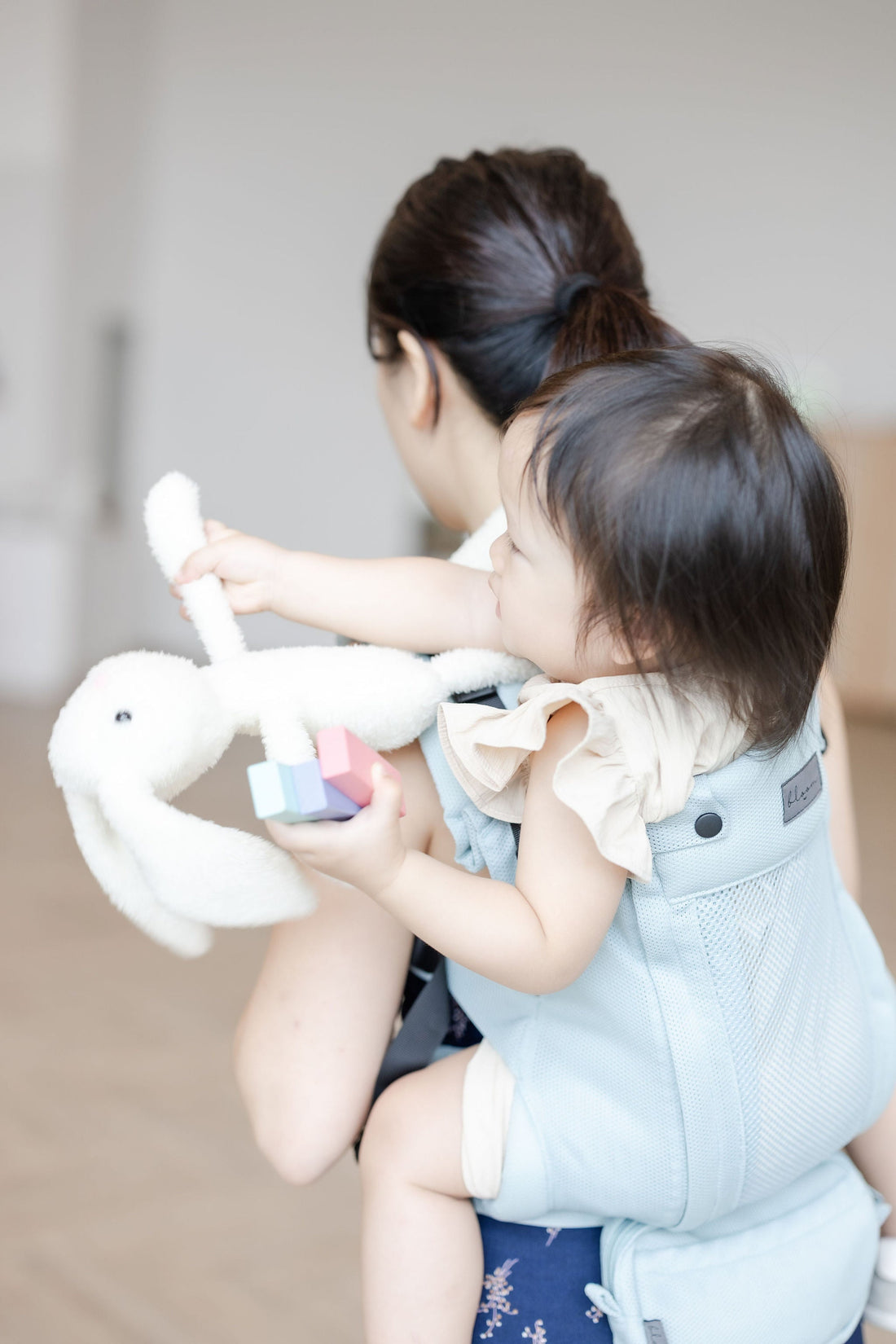 An asian mum back carrying her toddler using Tiny Bloom Club dusty blue coloured carrier